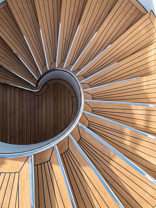 Sweeping teak spiral staircase with polished steel rail