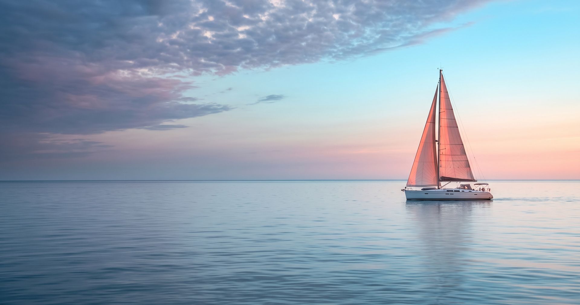 Lone sailboat with coral sails on mirror-calm water beneath a dusk sky