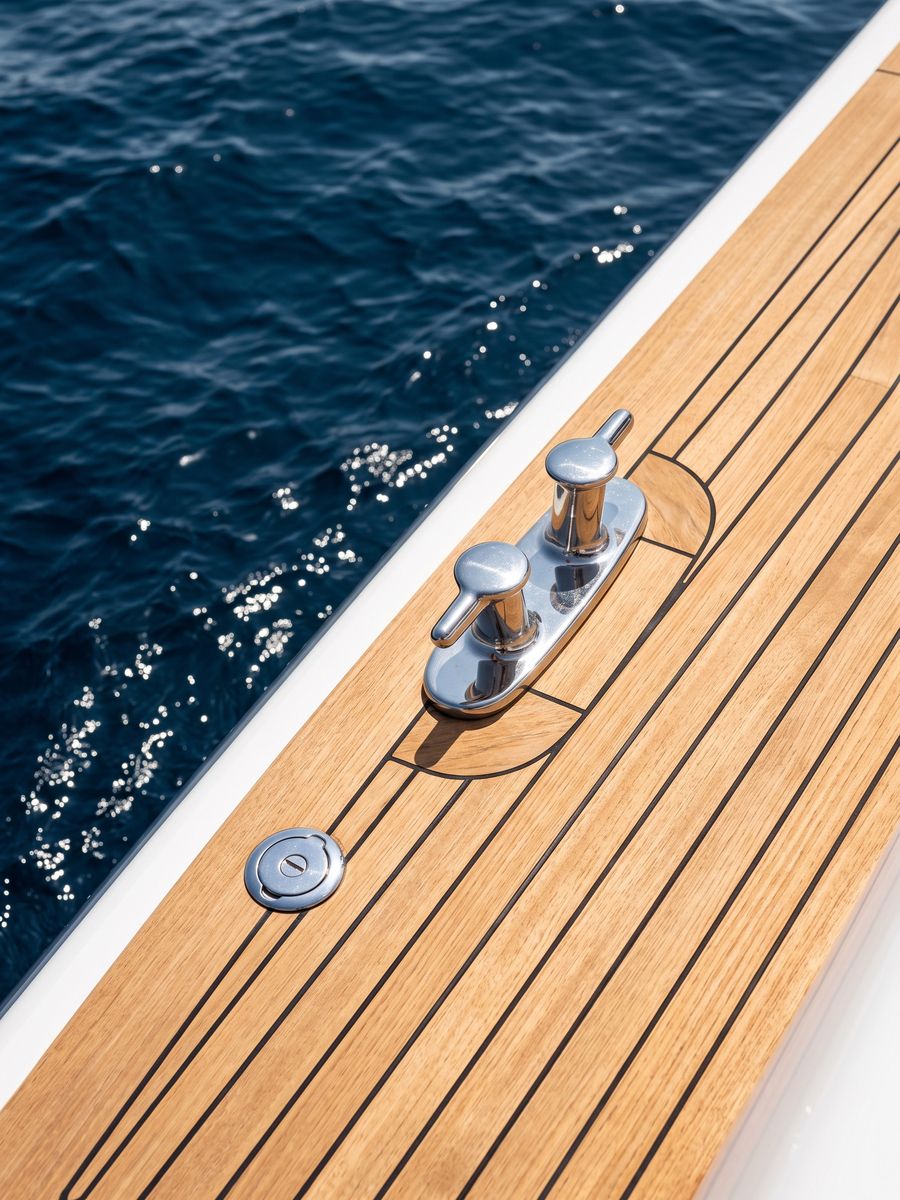 Polished chrome mooring cleat on a teak yacht deck above deep blue water